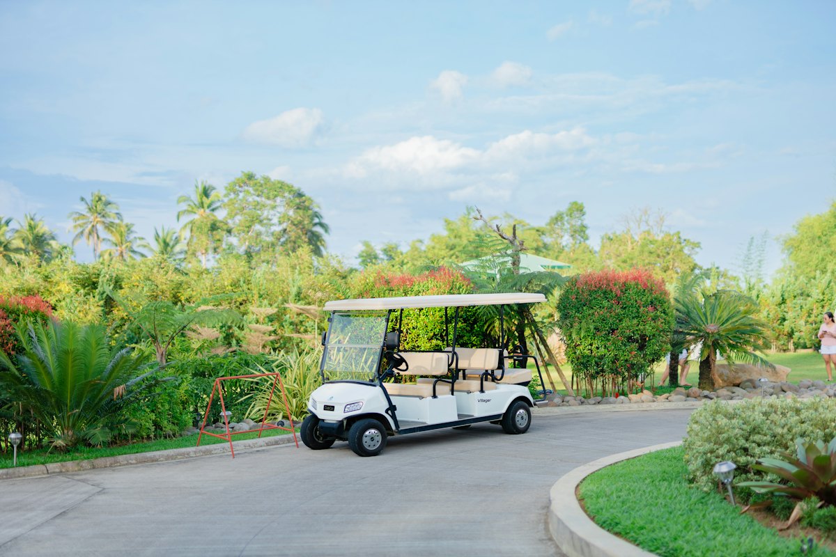A white six-seat golf cart parked on a paved drive among palms