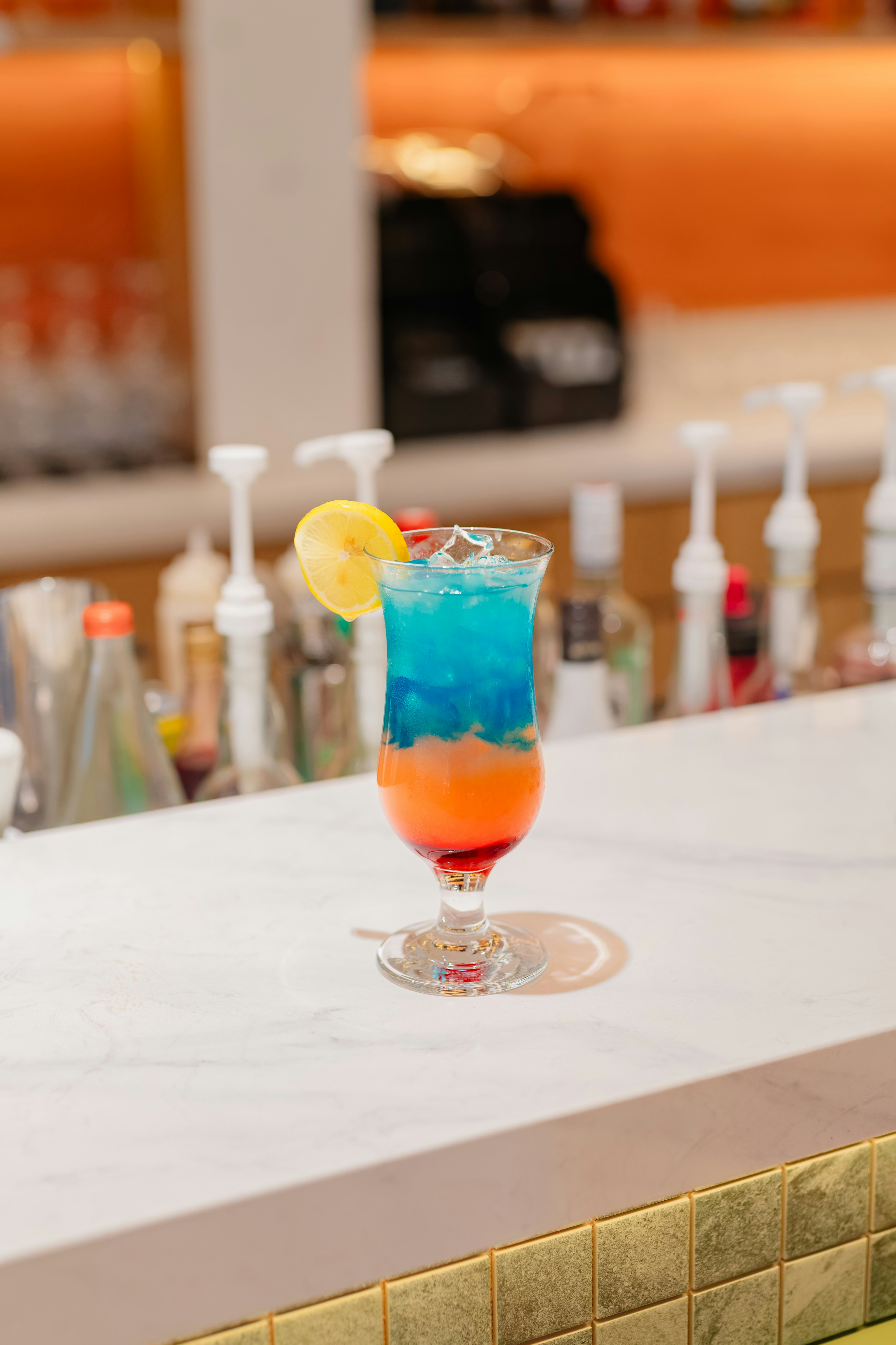 Bunter Schichtcocktail mit Zitronenscheibe an der Bar.