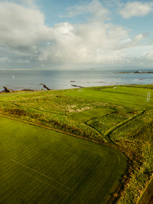 Green fields meet the ocean under a cloudy sky.