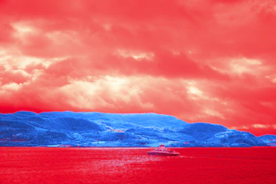 Red clouds over blue mountains and water with boat.