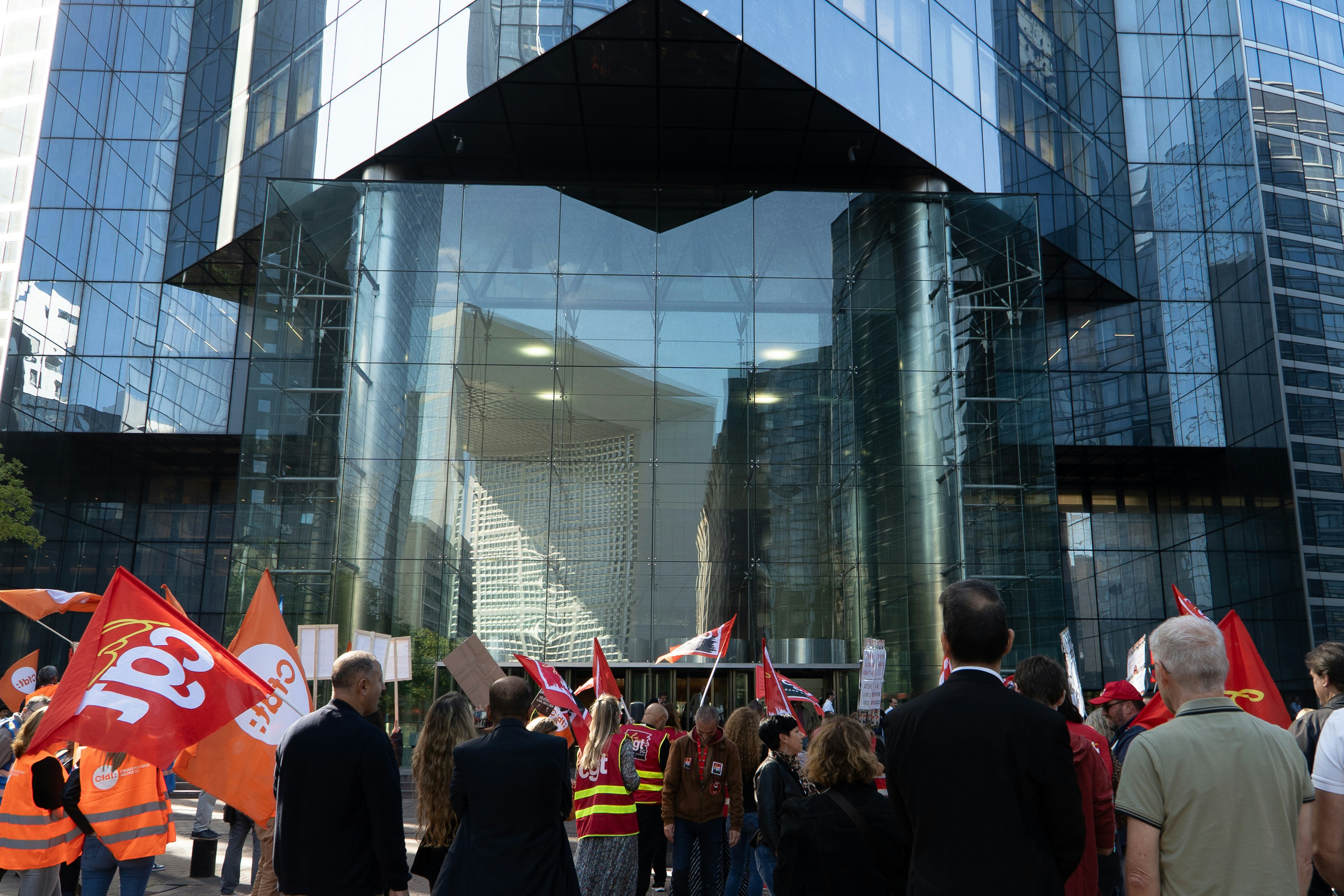 Protesters with flags gather in front of modern building