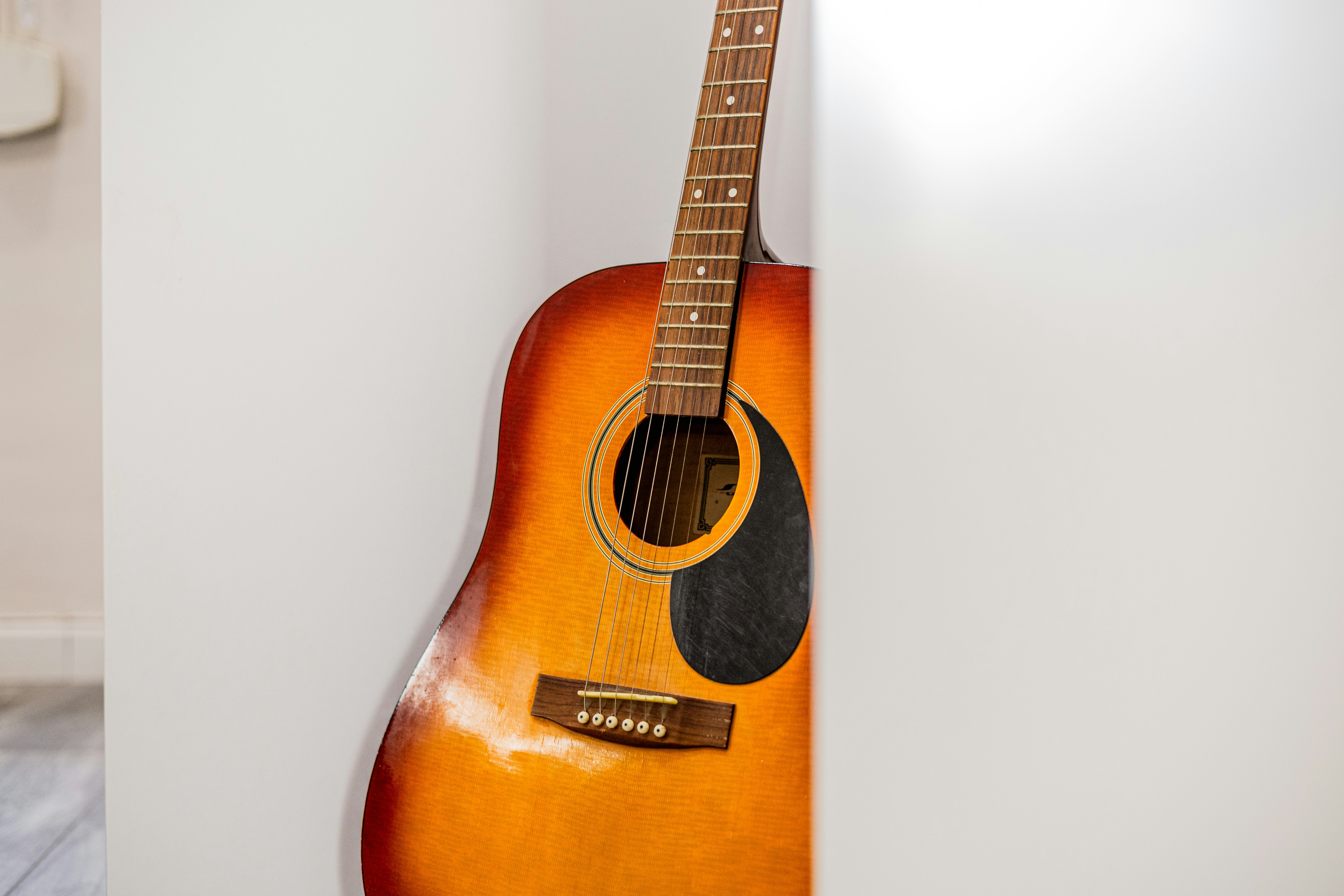 Acoustic guitar leaning against a white wall.