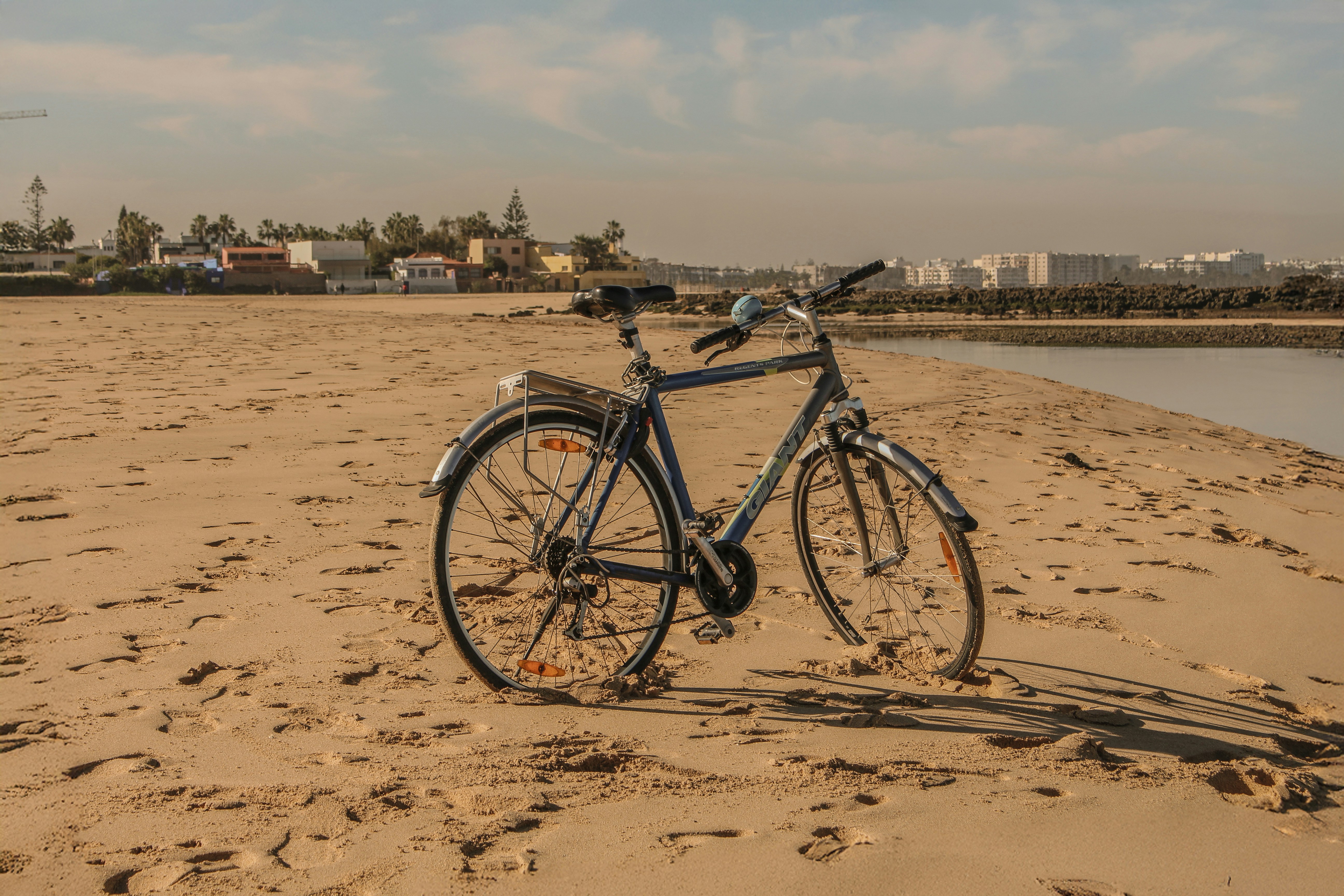 Bicycle parked on a sandy beach with buildings distant.