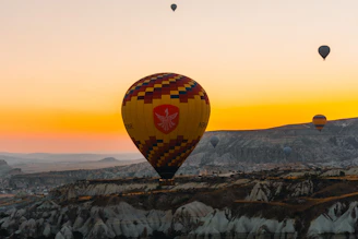 Hot air balloons float over rocky landscape at sunrise.