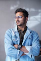 Man wearing glasses and denim jacket looking away.