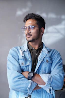 Man wearing glasses and denim jacket looking away.