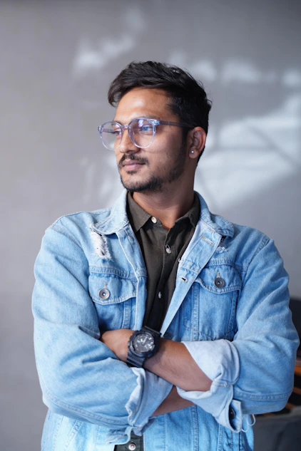 Man wearing glasses and denim jacket looking away.
