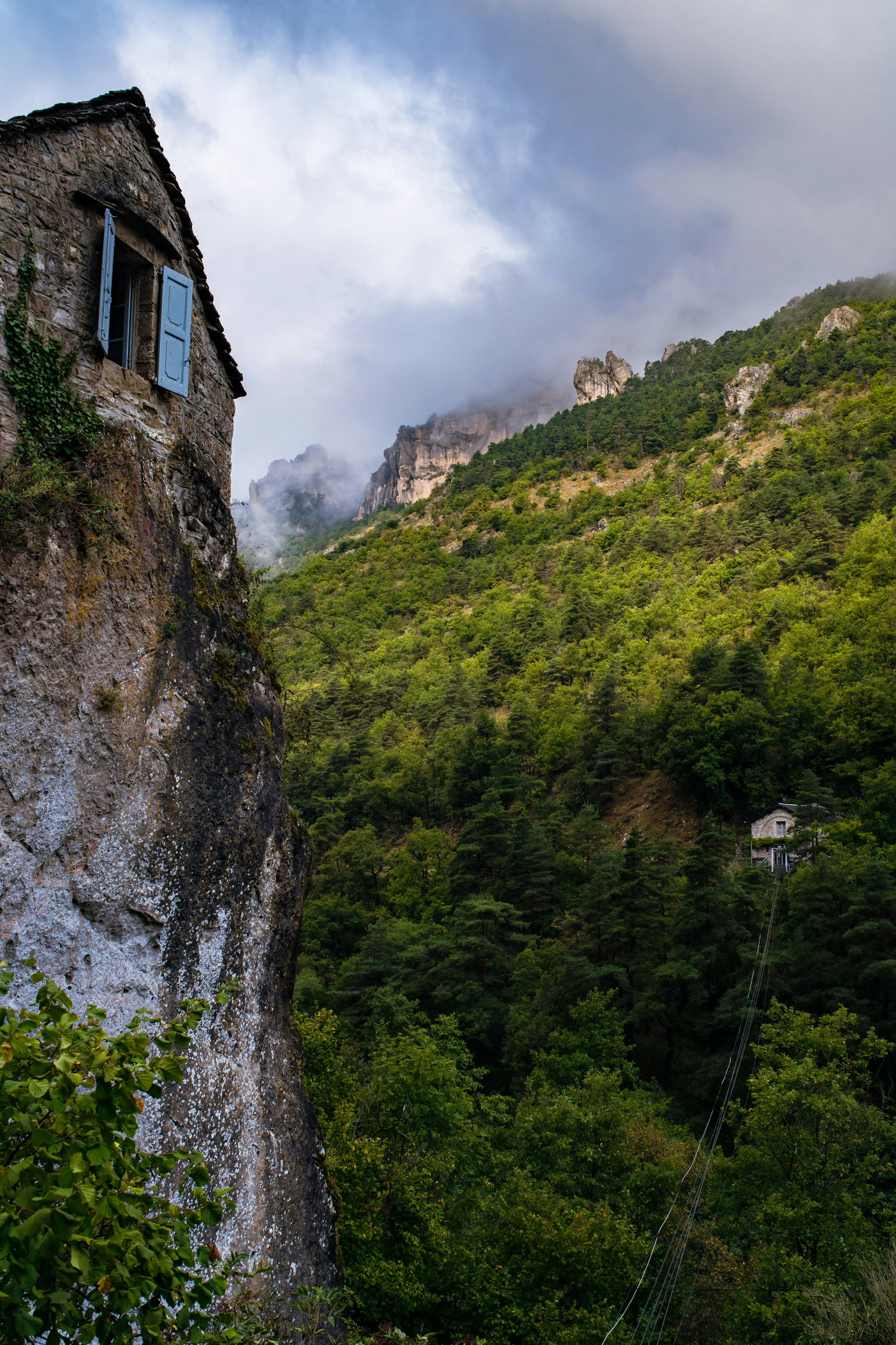 森に覆われた山々が続く岩だらけの崖の中腹に建てられた石造りの家。