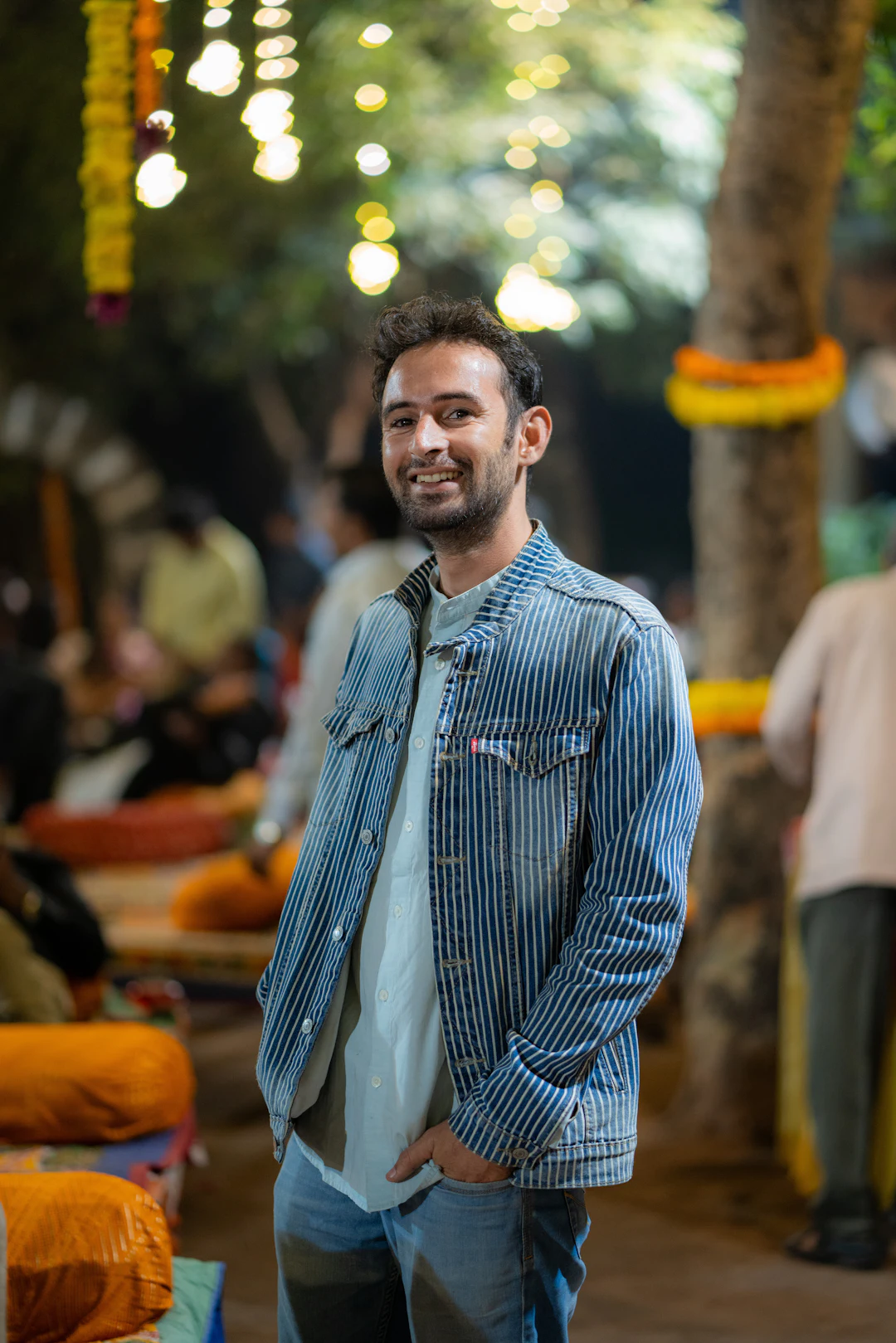 A smiling young man in a denim jacket at a neighbourhood market