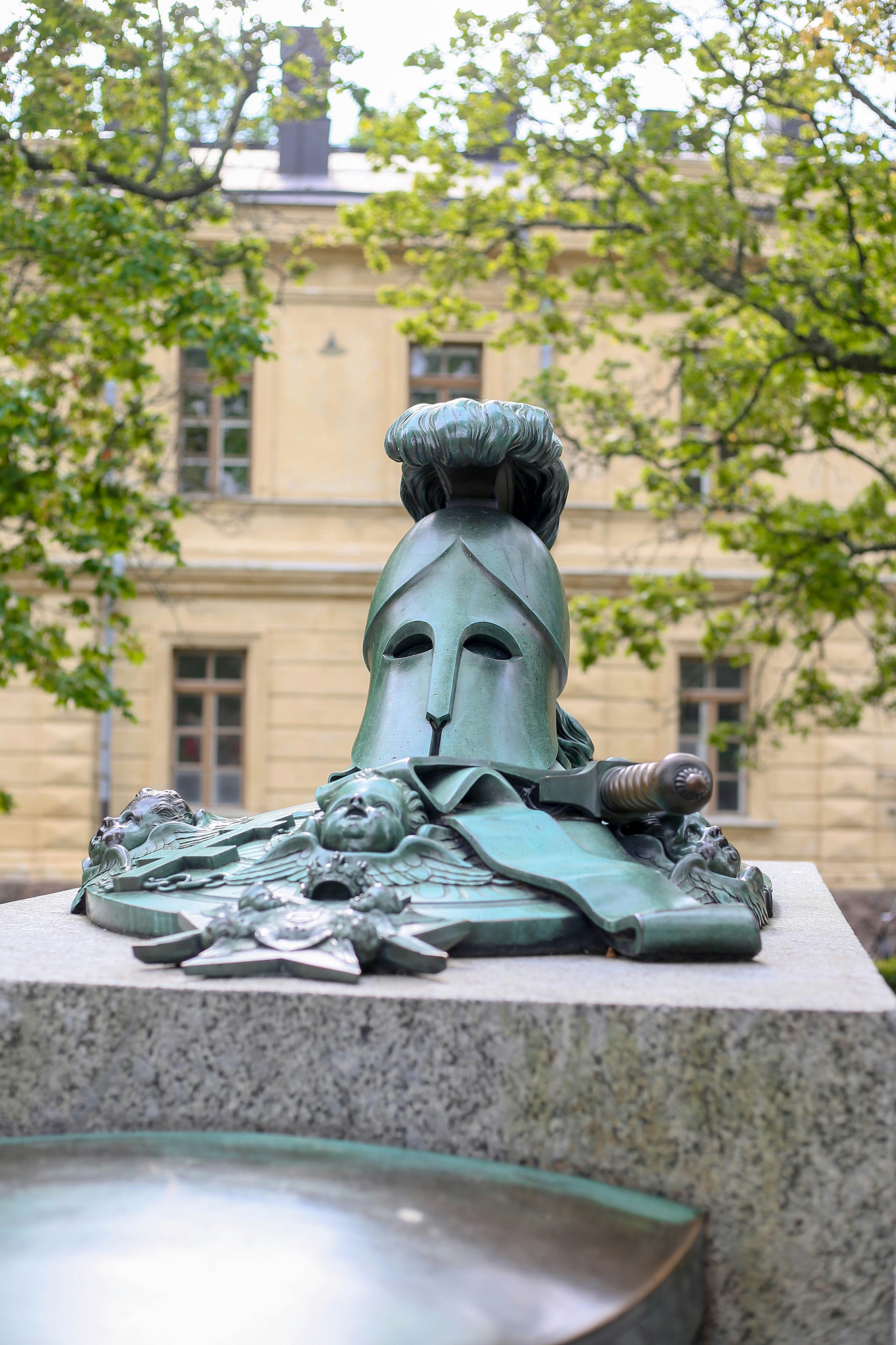 Bronze helmet sculpture with surrounding figures on pedestal