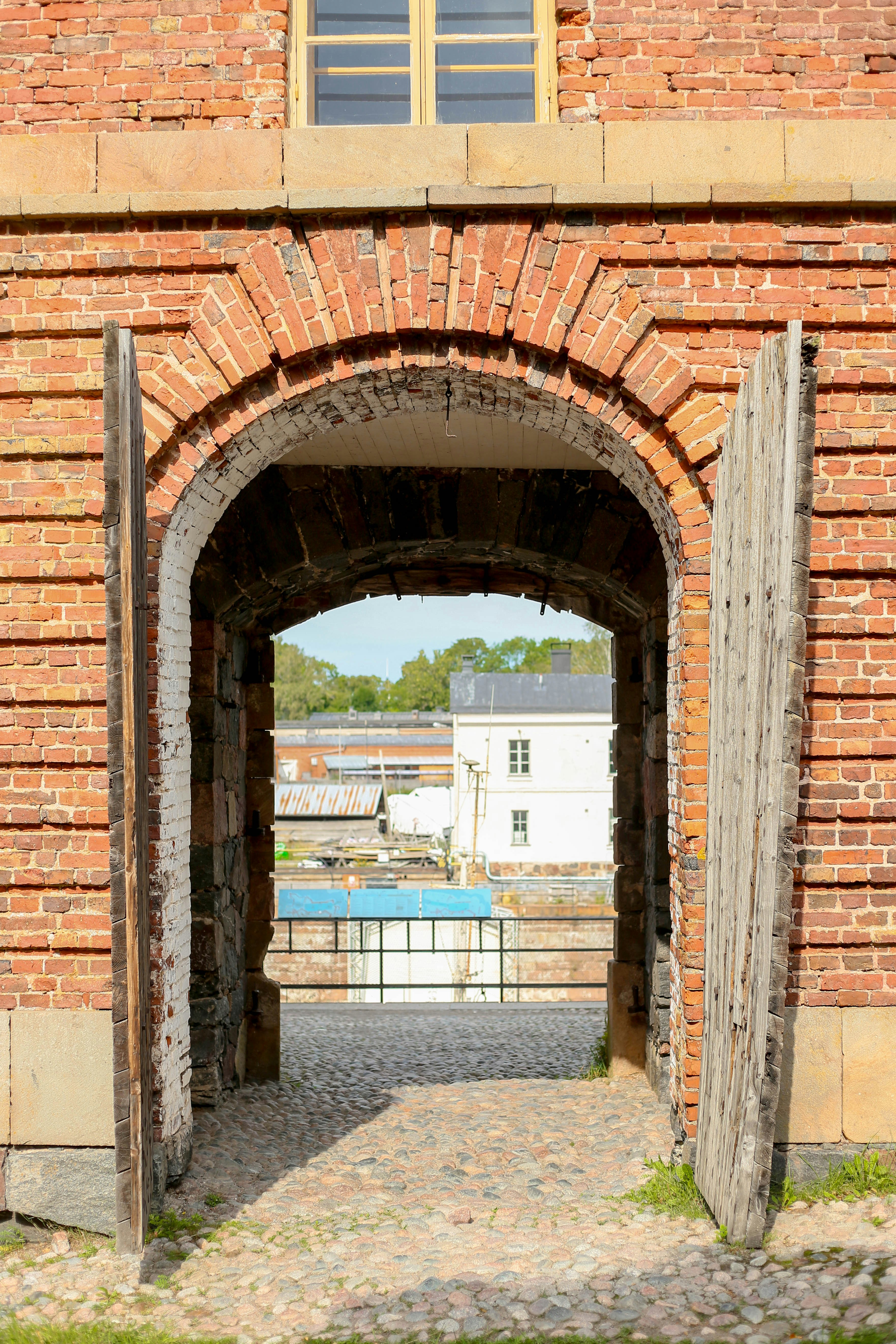Open wooden doors lead through brick archway to buildings