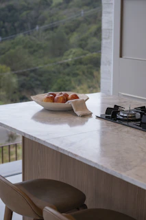 Bowl of apples on marble countertop with stove.