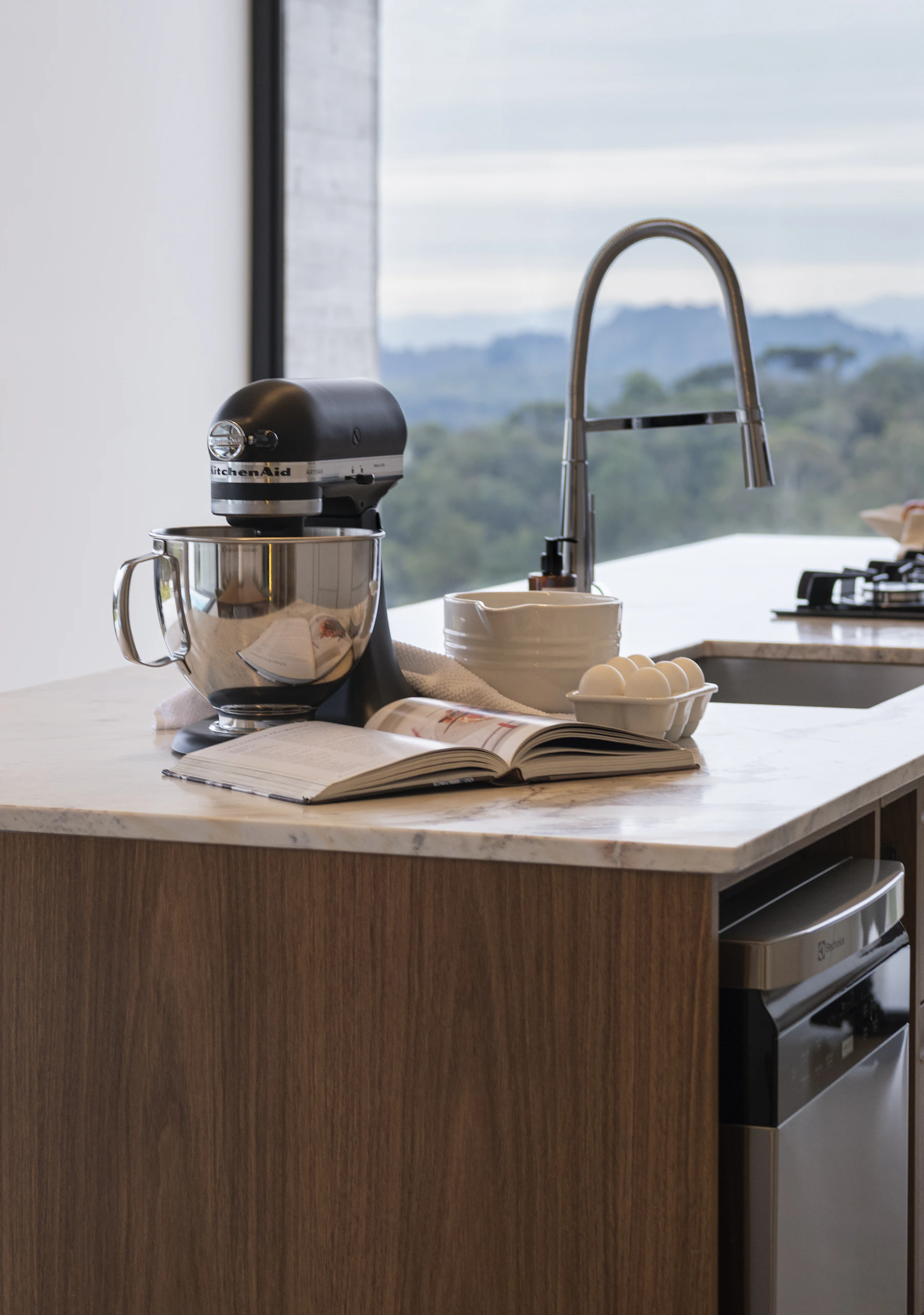 Stand mixer on a bright modern kitchen island with baking ingredients and an open recipe book