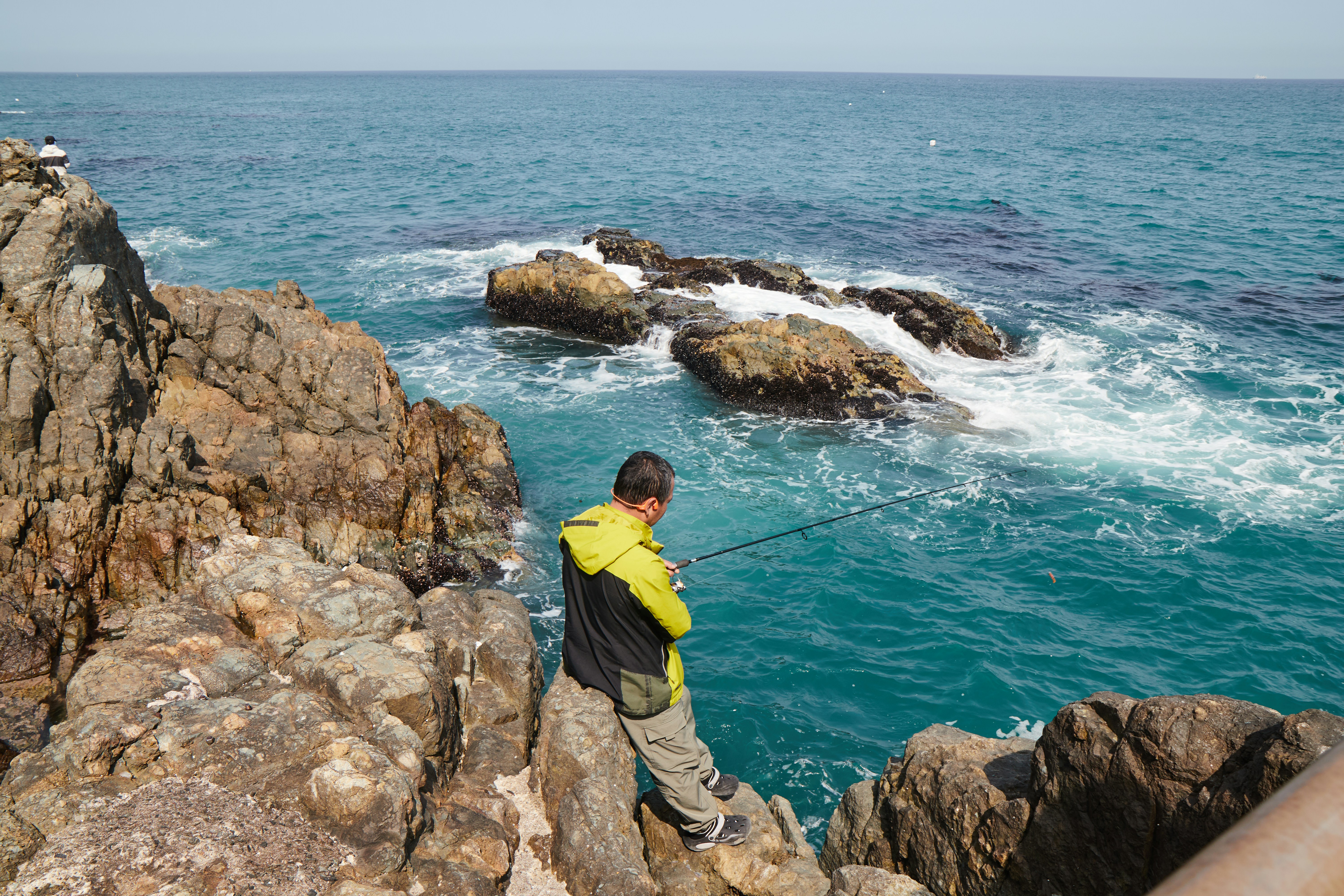 Man on rocky coast overlooking blue ocean waves