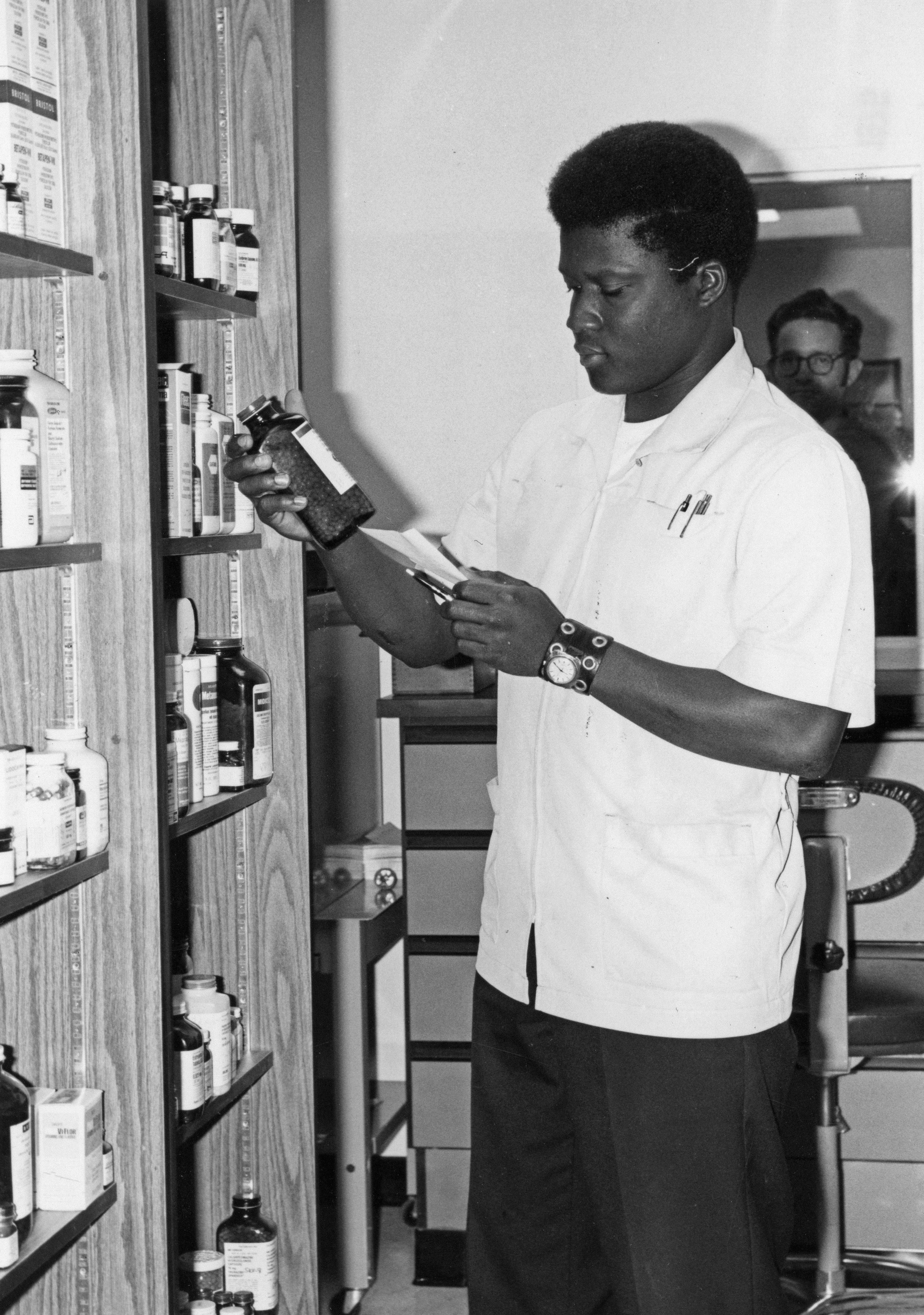 09-8048-107 HM [hospitalman] Huesont James fills a prescription. Branch Clinic, Naval Support Activity, Brooklyn, New York. [Pharmacy.] Hospital Corpsmen - in action. 11/1975.