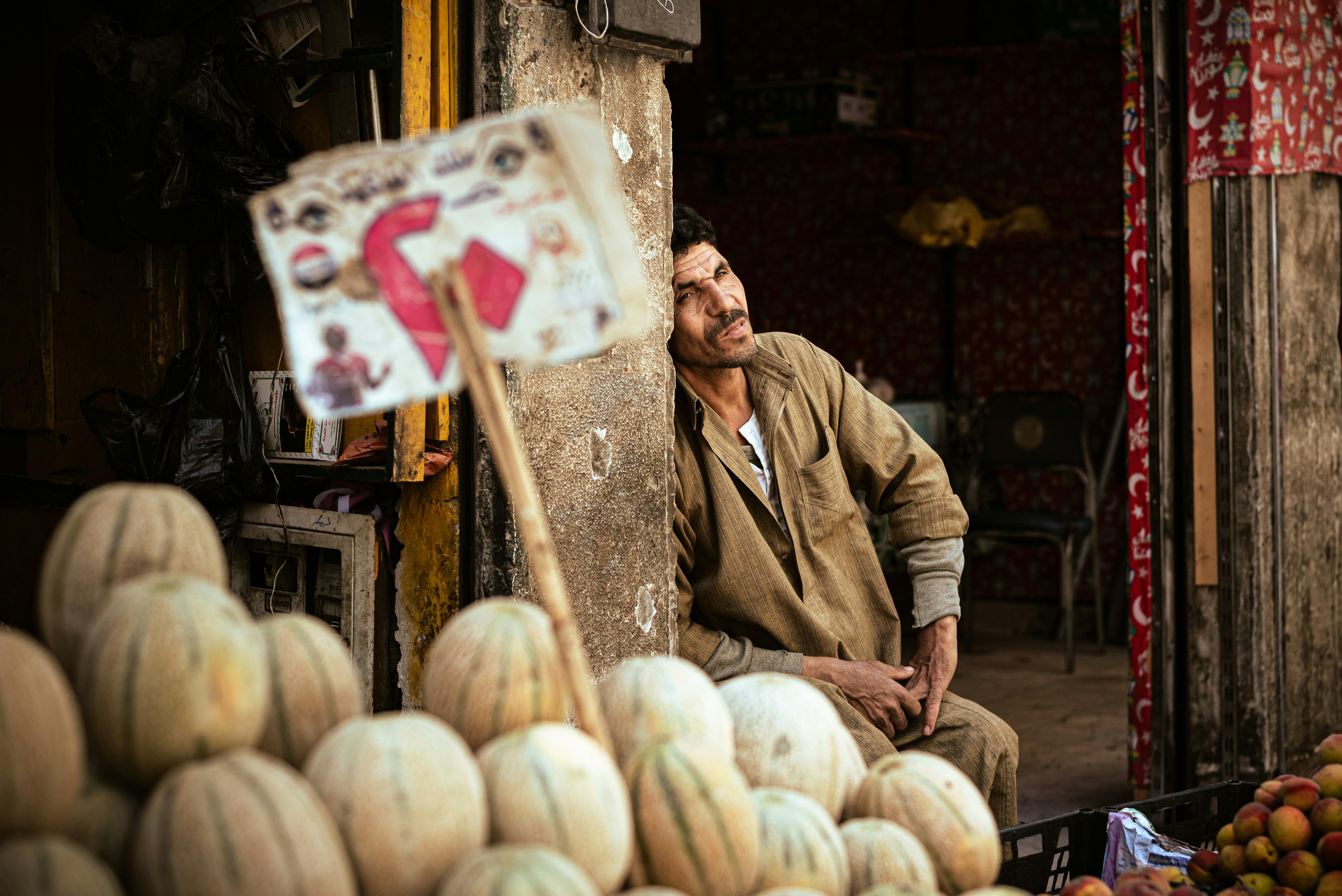 Man resting by a fruit stall with melons