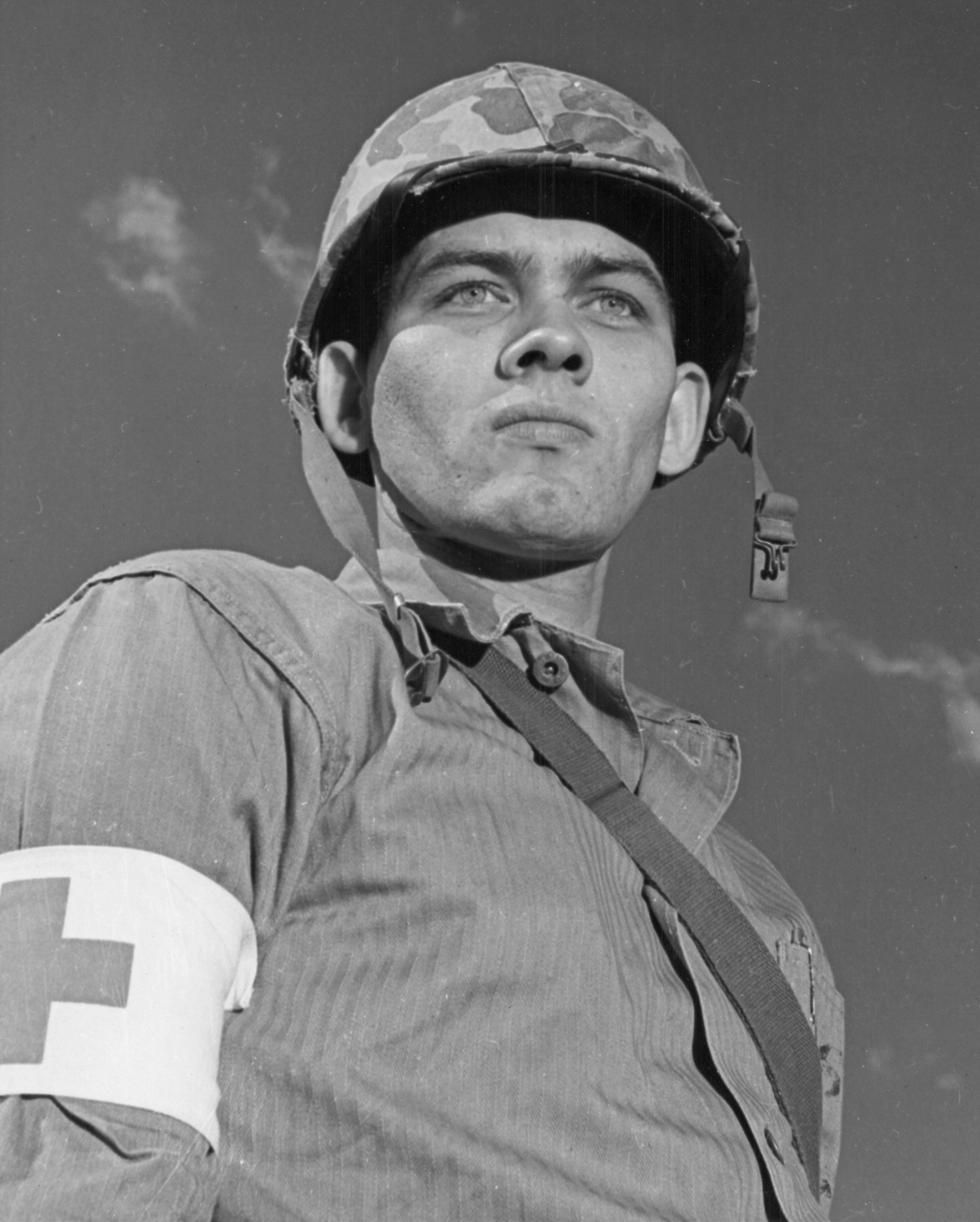 Soldier wearing helmet and red cross armband looks up
