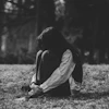 A person sits curled up on grassy ground