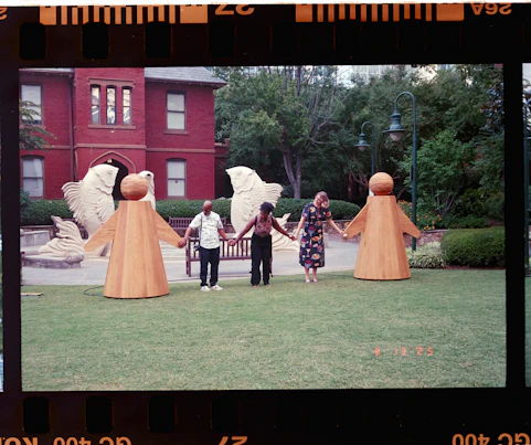 Three people hold hands between two large orange figures.
