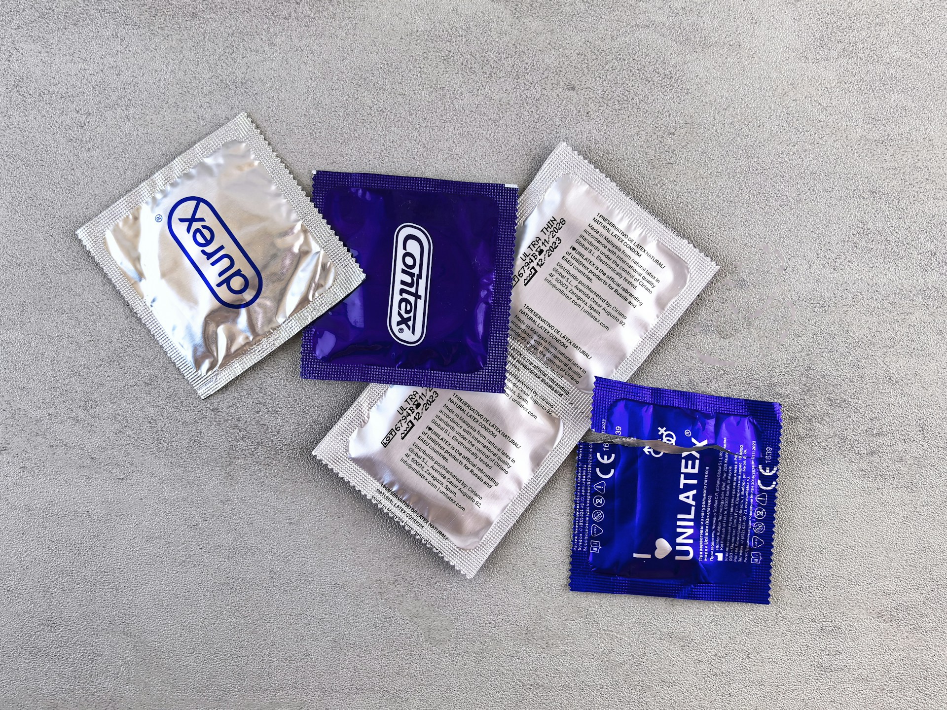Several individually wrapped condoms on a gray surface.