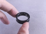 Fingers hold a black smart ring with circuits visible.