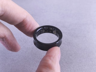 Fingers hold a black smart ring with circuits visible.