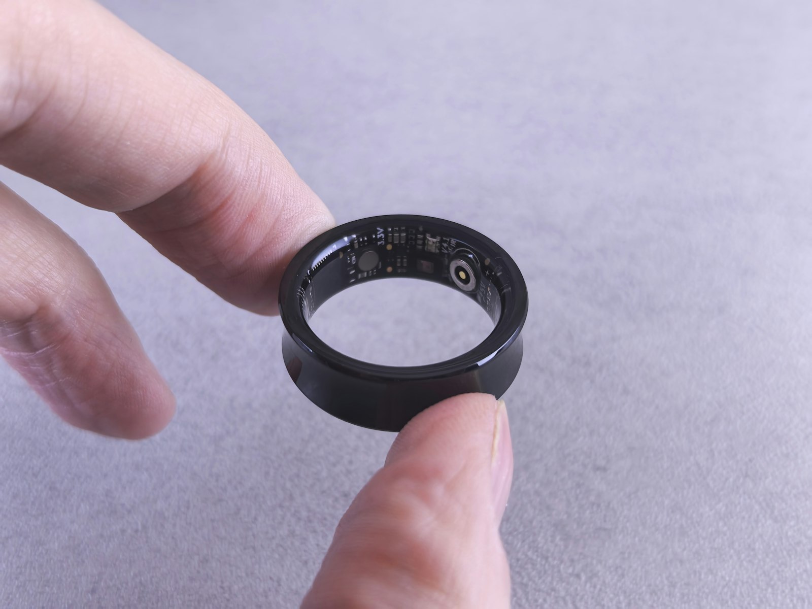 Black smart ring held in fingers, circuit detail visible, minimalist product shot