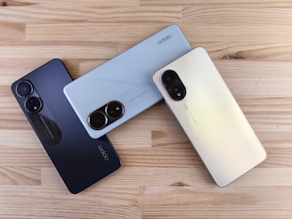 Three smartphones in different colors on a wooden surface