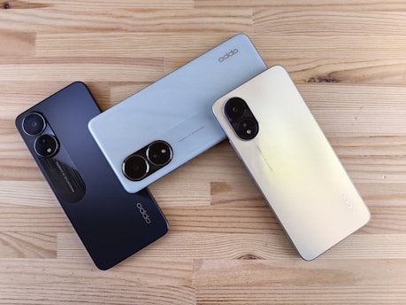 Three smartphones in different colors on a wooden surface