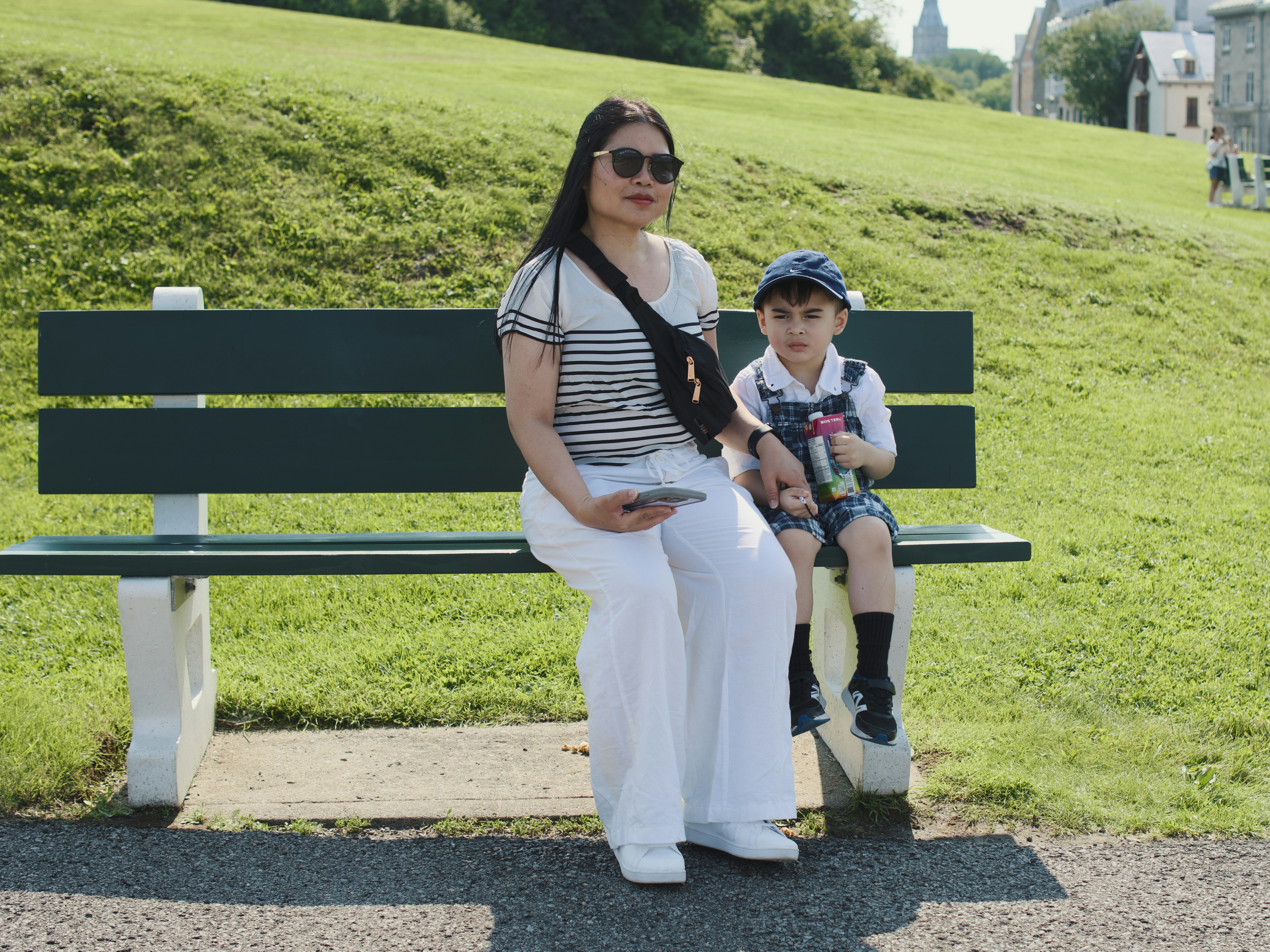 Woman and child sit on park bench in summer.