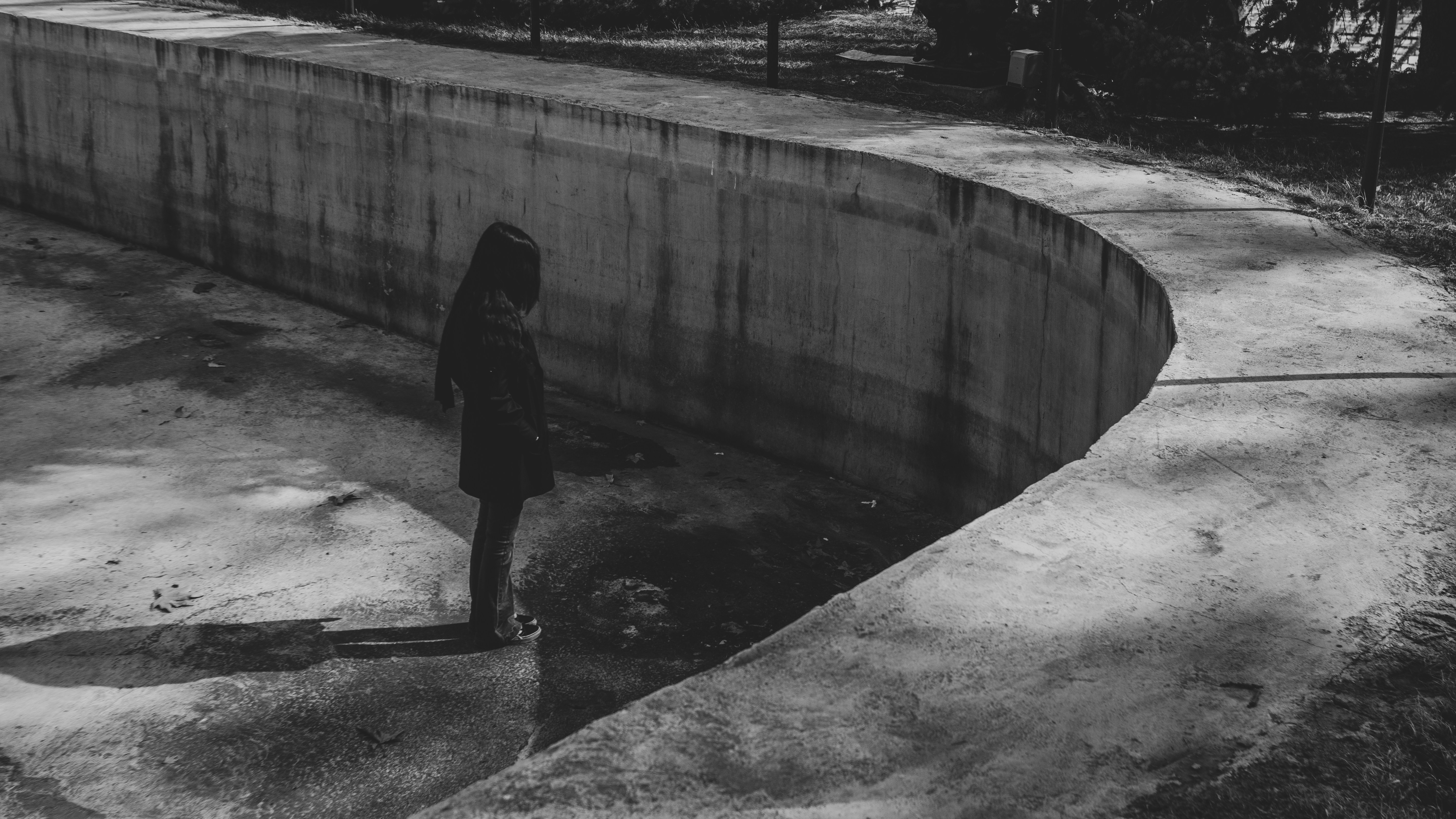 A solitary figure stands in an empty concrete basin.