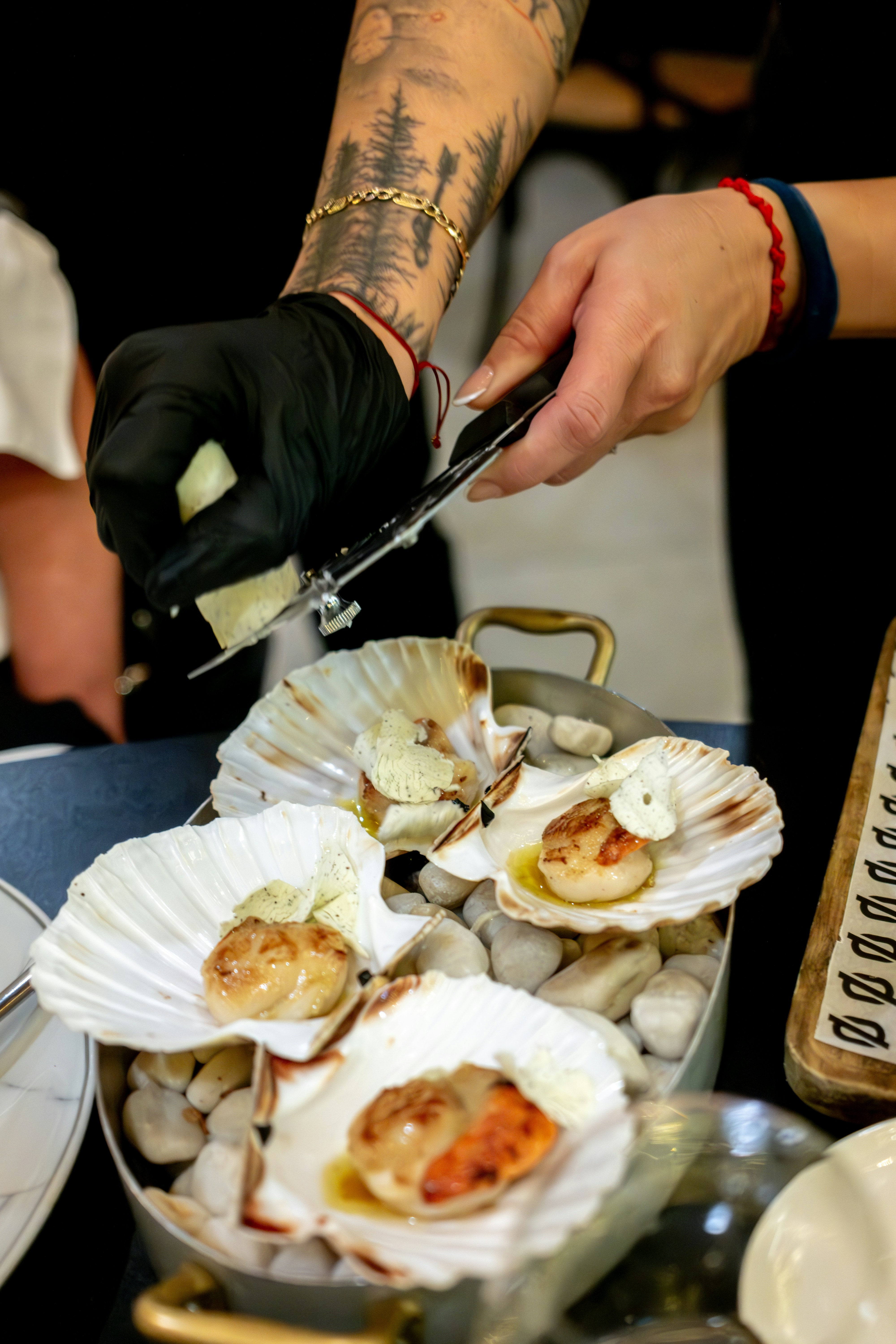 Chef grating cheese over seared scallops in shells.