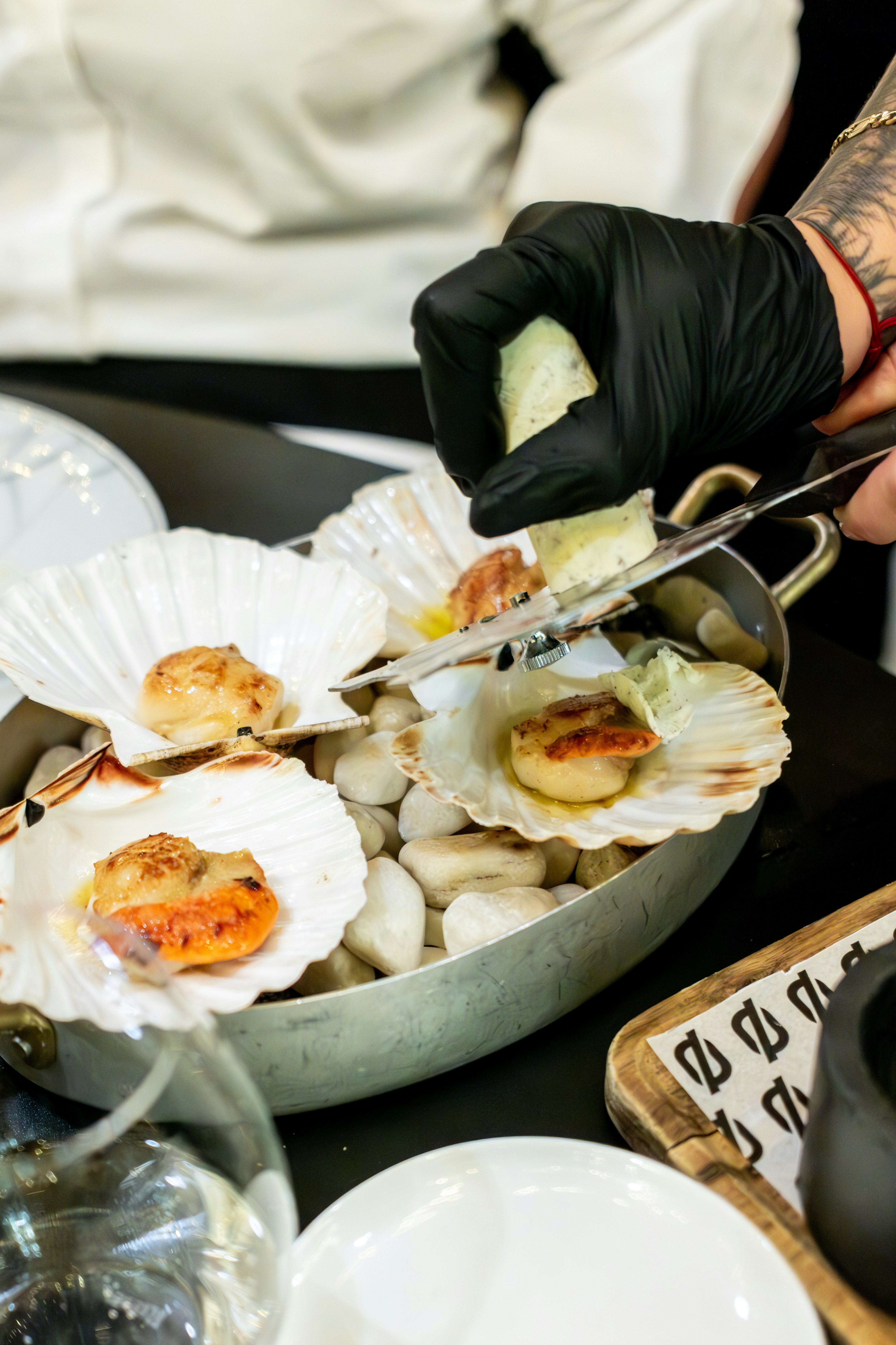 Chef garnishes seared scallops in shells with lemon.