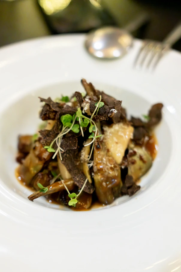 Gourmet dish with mushrooms and microgreens in white bowl.