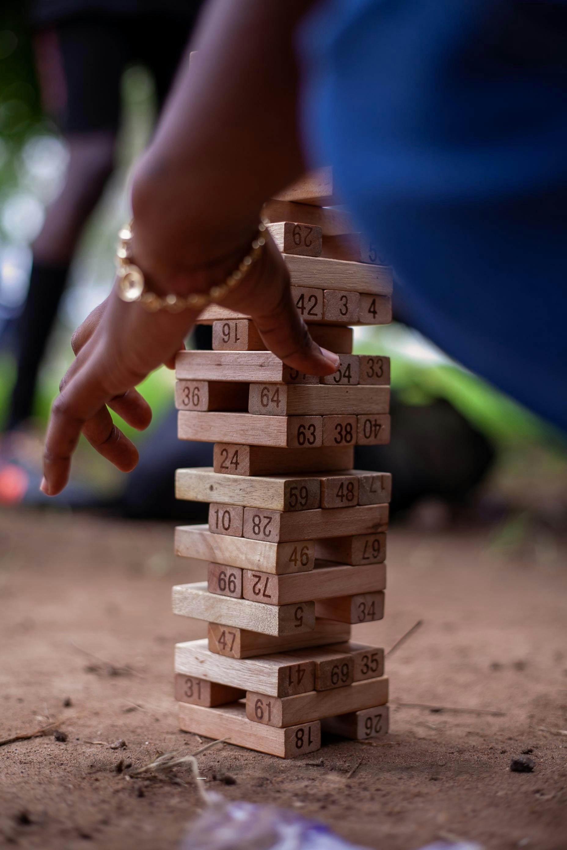Hand carefully removes block from tall wooden tower