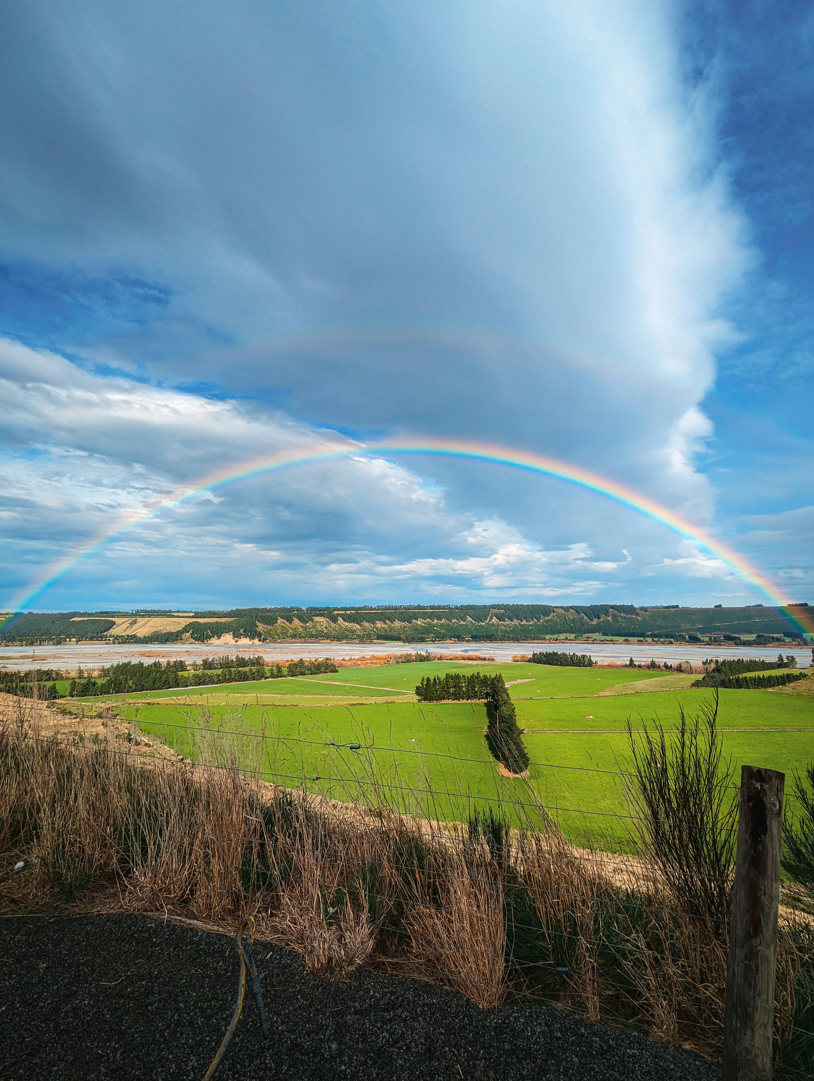 A rainbow arcs over green fields and a river.