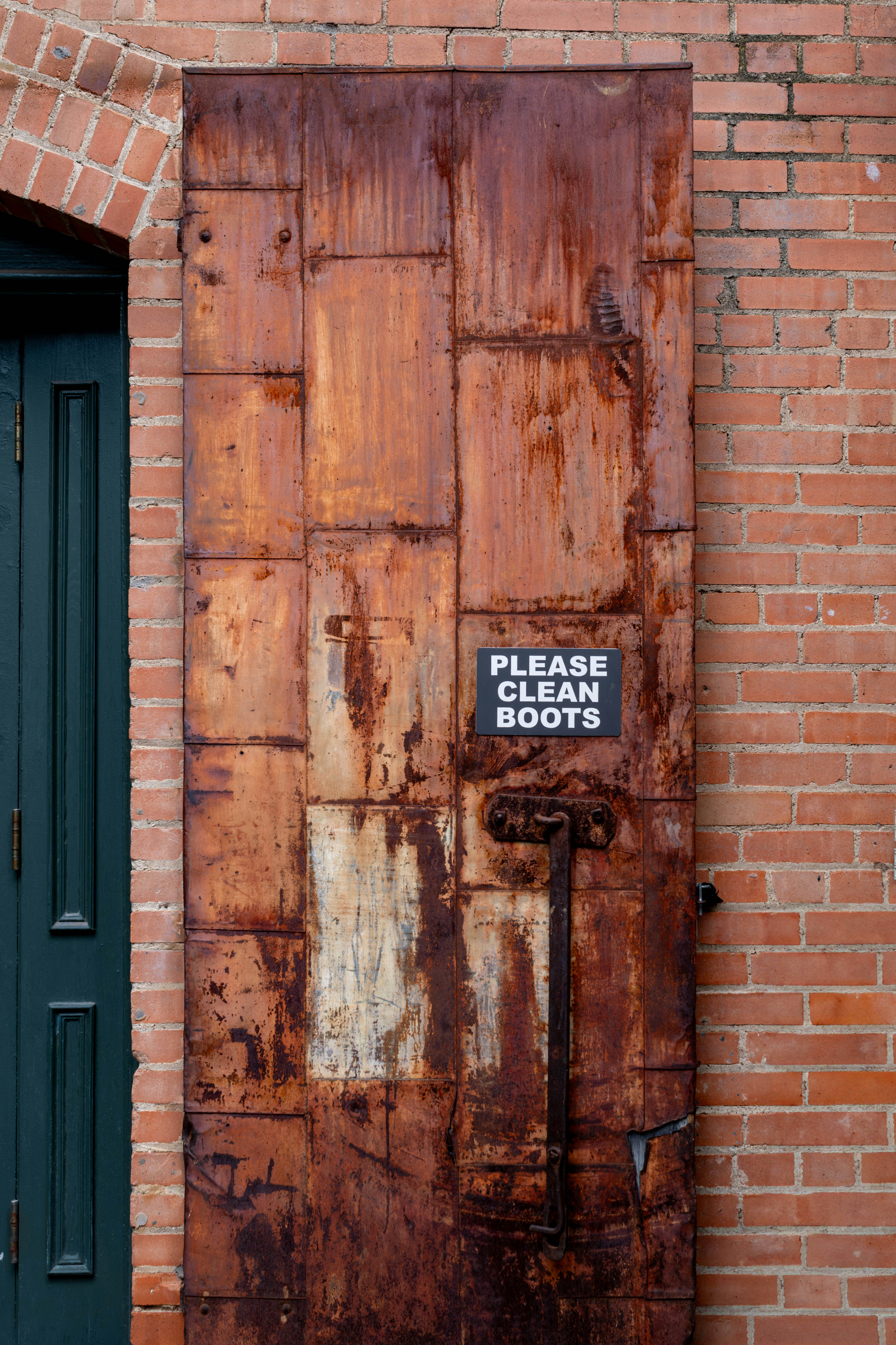 Rusted metal door with a "please clean boots" sign.