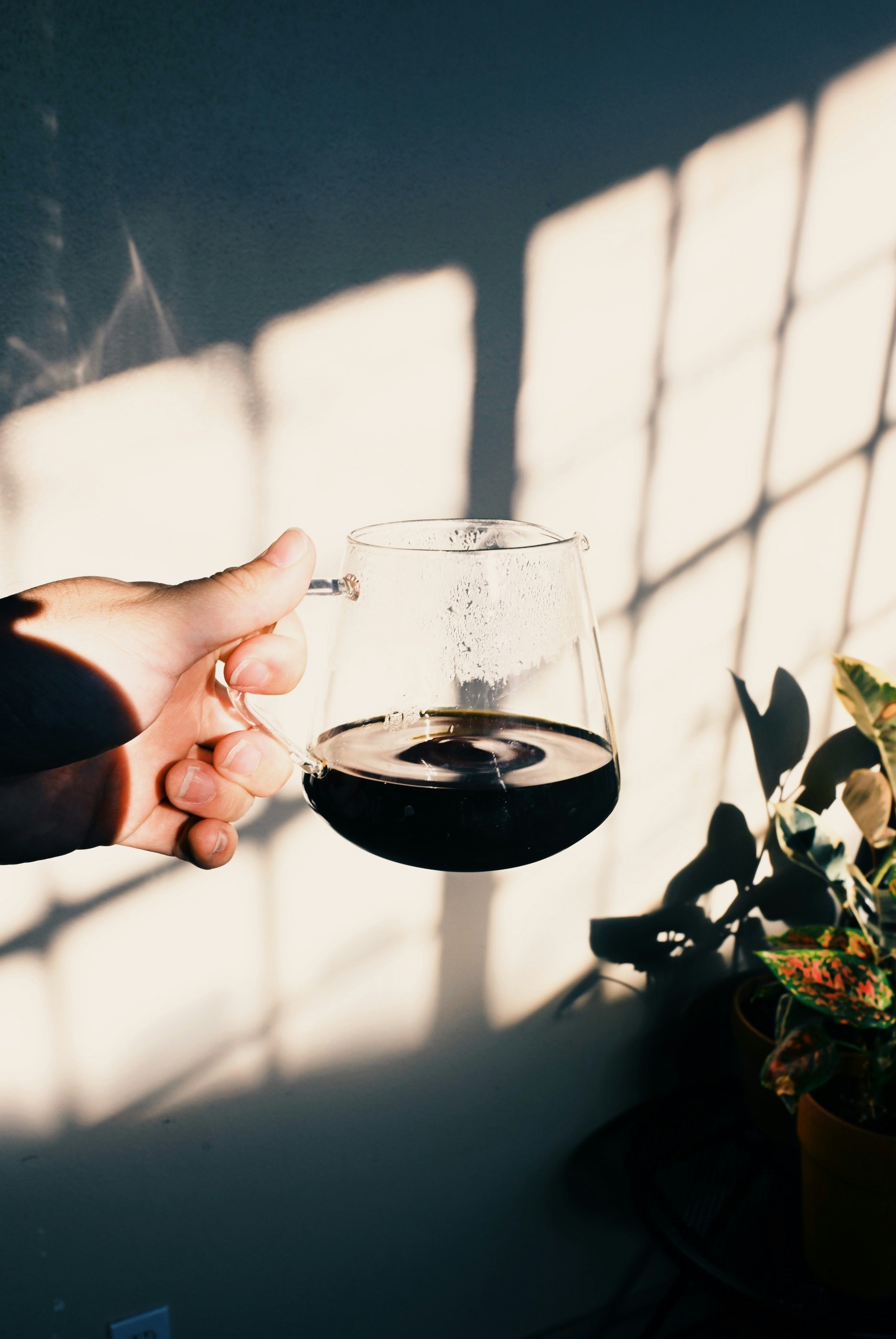 Mano sosteniendo una taza de vidrio de café oscuro.