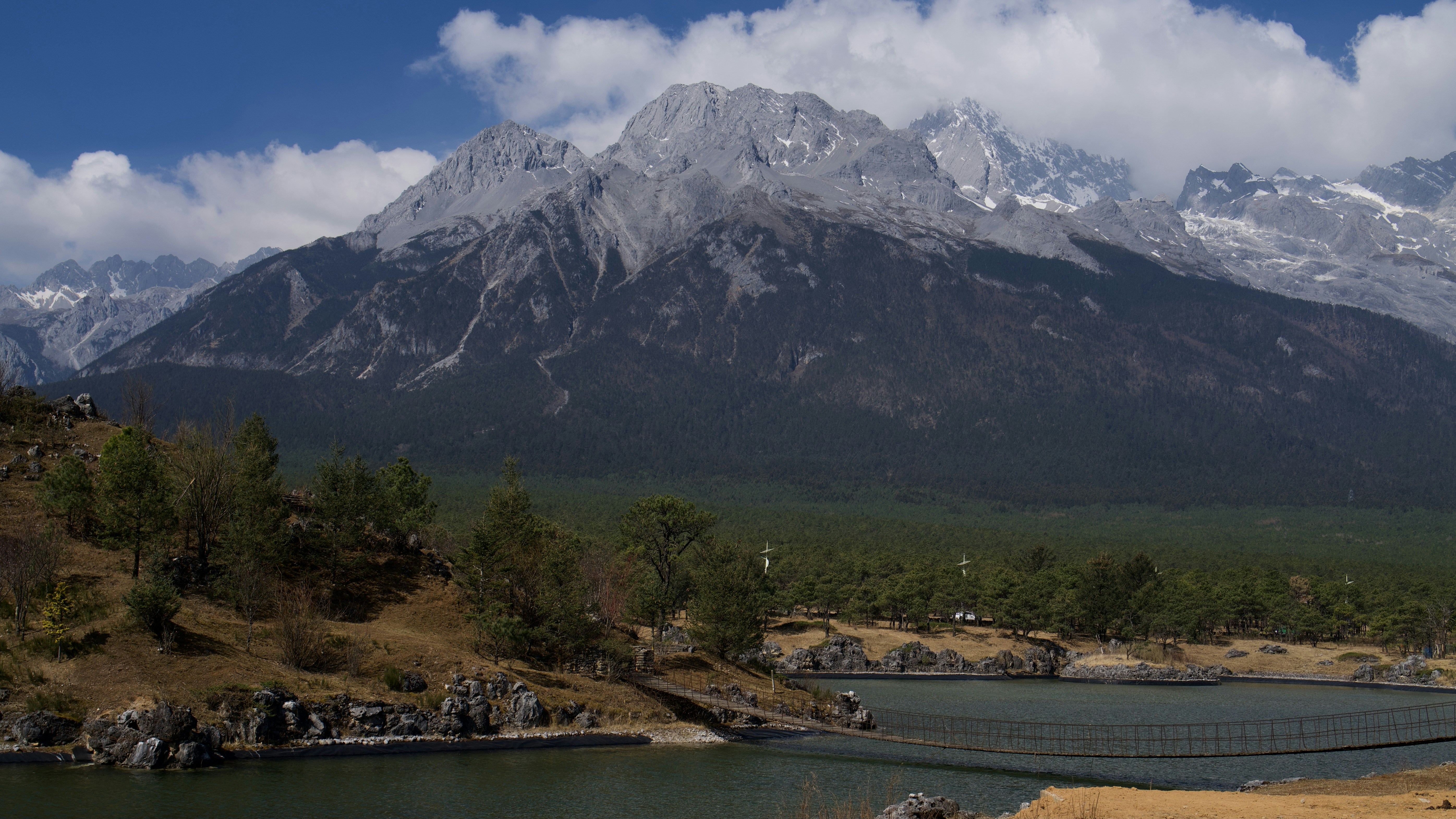 Snow-capped mountains rise above a serene lake and forest.