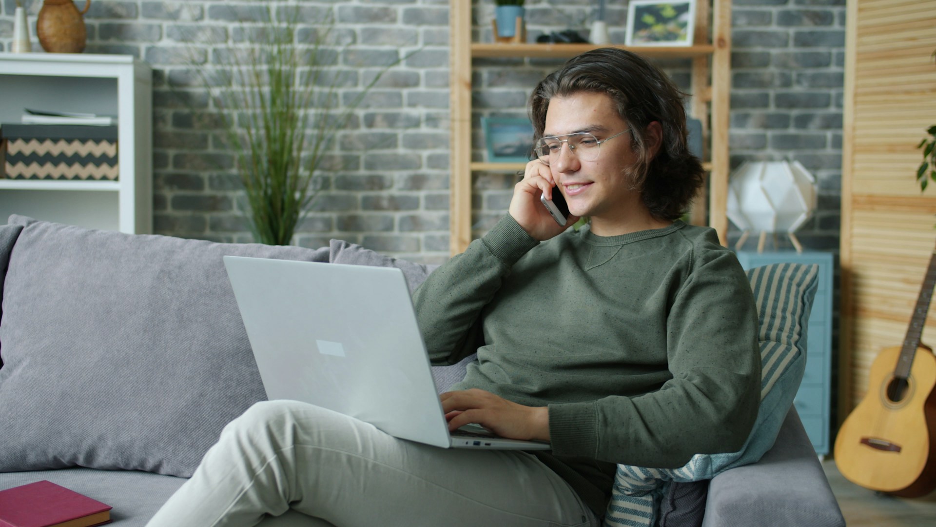 Man talking on phone while using laptop on couch