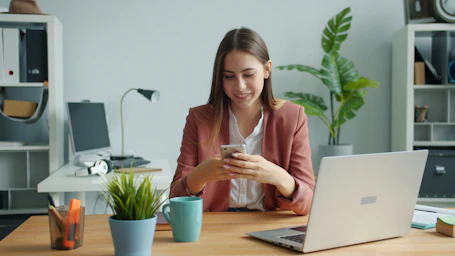Young woman smiling while using her smartphone at desk.
