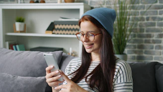 Young woman wearing a beanie and glasses using phone.