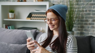 Young woman wearing a beanie and glasses using phone.