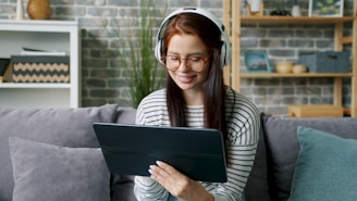 Young woman wearing headphones uses a tablet on couch.