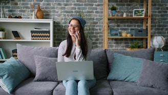 Woman talking on phone with laptop on couch.