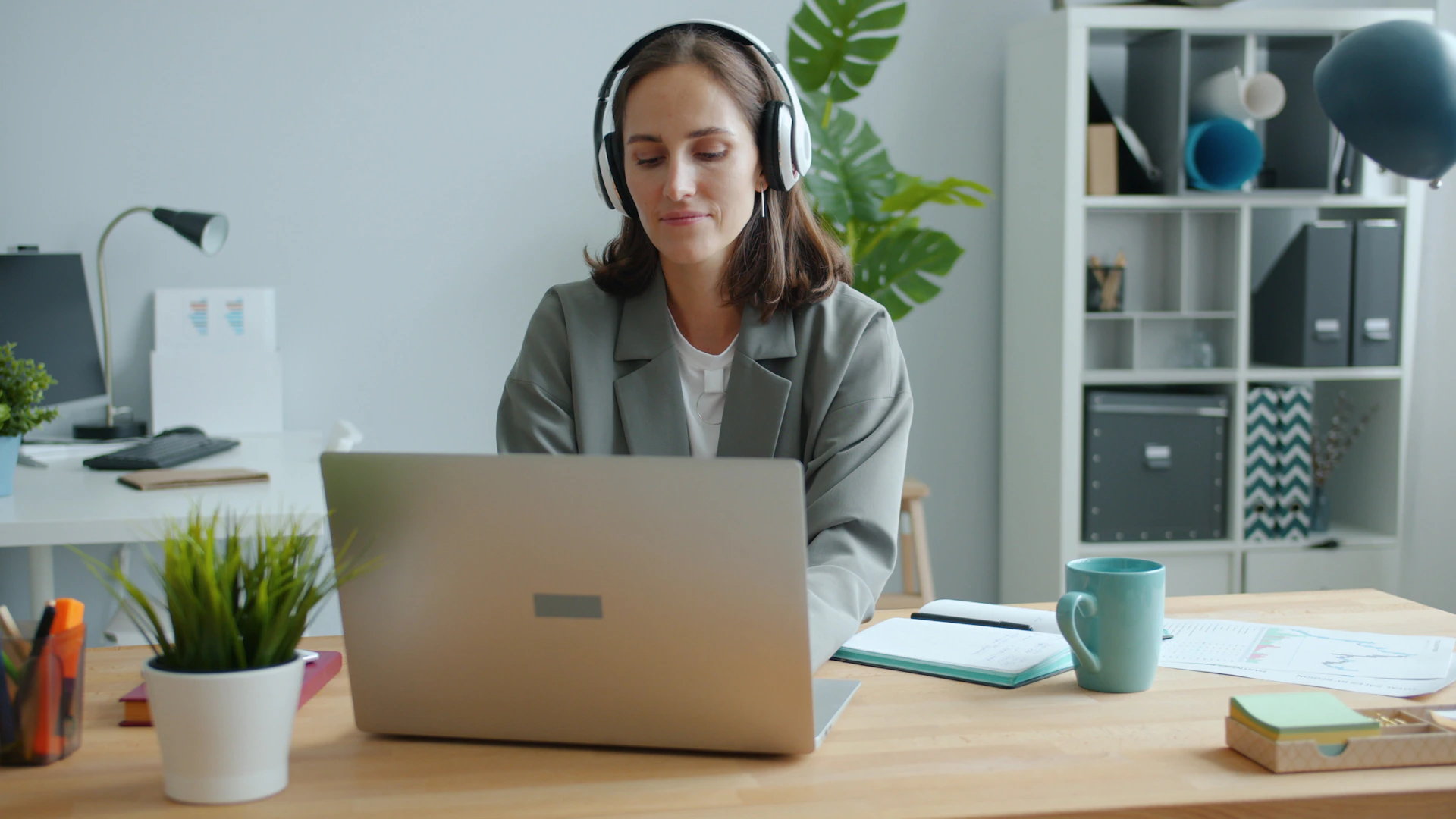 Woman wearing headphones works on laptop at desk