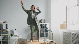 Woman in suit dancing on desk with headphones