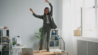 Woman in suit dancing on desk with headphones on