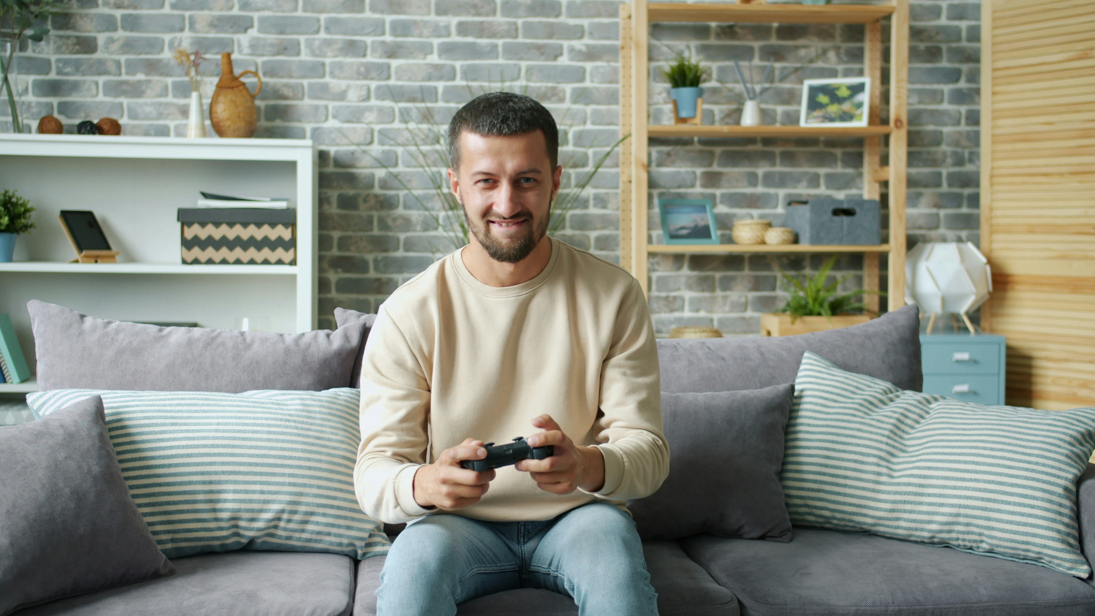 Portrait of cheerful carefree guy playing computer game in house alone looking at camera holding joystick having fun. Lifestyle and entertainment concept.