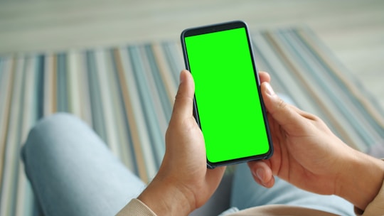 Hands holding a smartphone with a green screen.